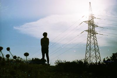 Low angle view of silhouette woman standing by electricity pylon on field against sky