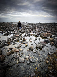 Rear view of person on rocks at beach against sky