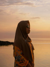 Woman standing at beach against sky during sunset