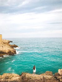 Rear view of woman standing against sea on rock