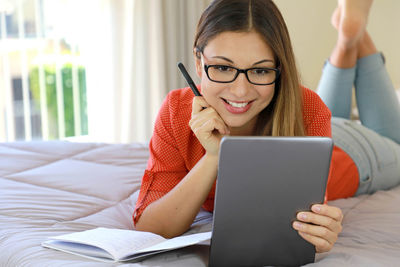 Young woman using digital tablet while lying on bed at home