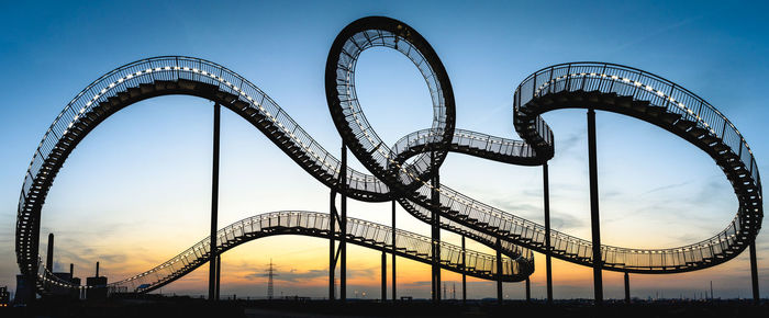 Low angle view of illuminated rollercoaster against sky during sunset