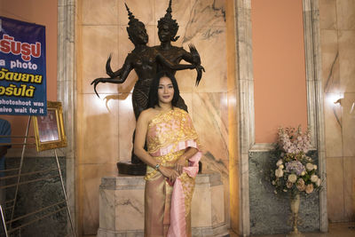 Portrait of young woman wearing traditional clothing standing against statues