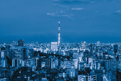 Illuminated buildings in city against blue sky