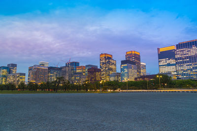 Illuminated buildings in city against cloudy sky