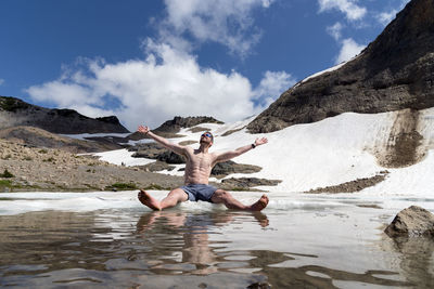 Man sitting in lake against mountains during winter