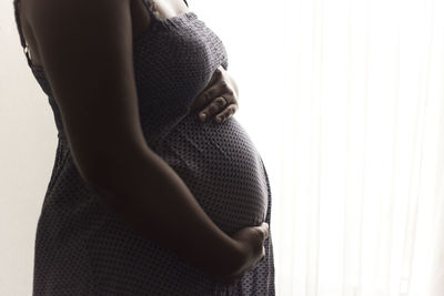 Midsection of pregnant woman touching abdomen against white background