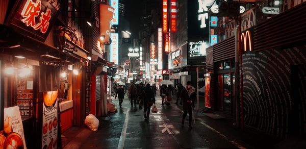 People walking on illuminated street amidst buildings at night