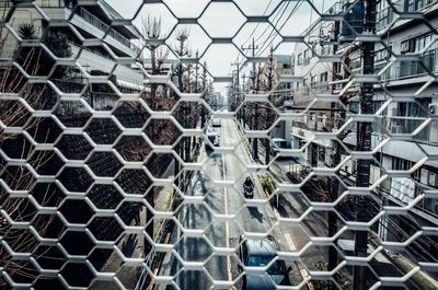 Road amidst buildings in city seen through metal grate