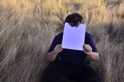 Rear view of man reading book on field