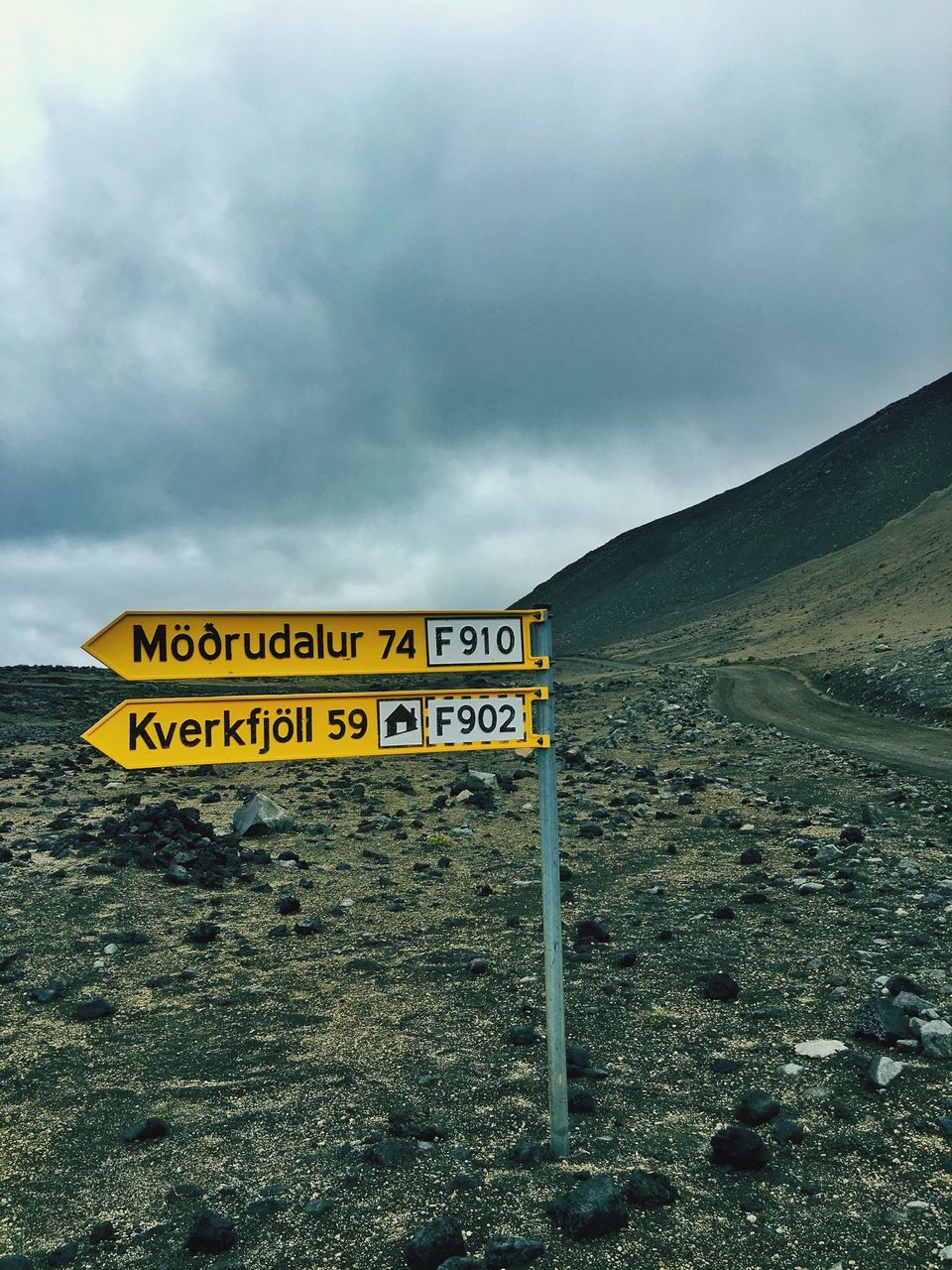 text, western script, communication, information sign, yellow, information, sky, symbol, signboard, cloud, outdoors, sign board, day, cloud - sky, journey, mountain, no people, cloudy