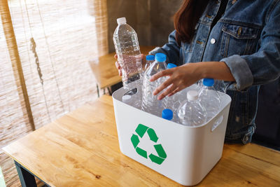 Midsection of woman holding bottle on table