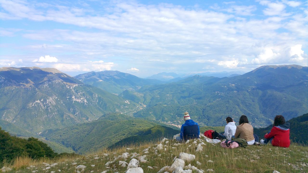 mountain, leisure activity, lifestyles, sky, mountain range, men, landscape, scenics, person, tranquil scene, cloud - sky, tranquility, sitting, beauty in nature, rear view, nature, casual clothing, vacations, full length