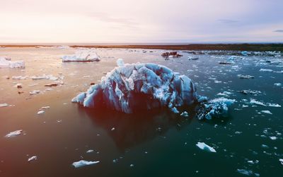 Frozen sea shore against sky during sunset