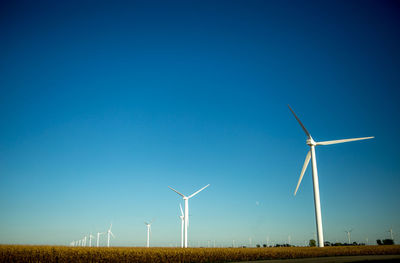 Wind turbines on field against clear blue sky