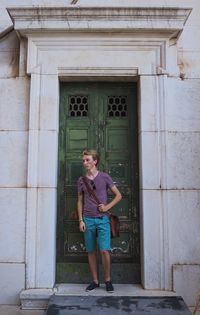 Full length of young man standing by closed green doors