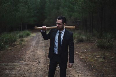 Young businessman with axe standing on dirt road in forest