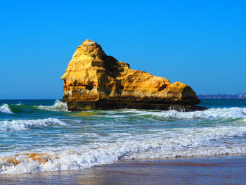 Rock formation on beach against clear blue sky
