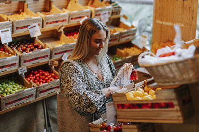 Smiling woman choosing tomatoes in shop