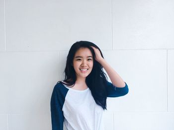 Portrait of smiling young woman standing against wall