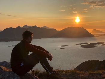 Man sitting on mountain against sky during sunset