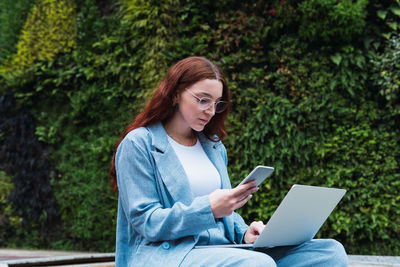 Red head business woman reading text message from her managers outdoors while using laptop