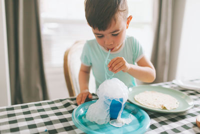 Boy playing with milk while sitting on table at home