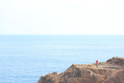Distant view of man standing on rocky mountain against sea