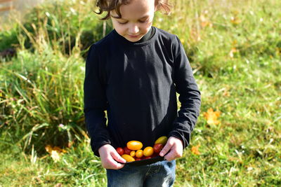 Boy holding fruits while standing on grassy field