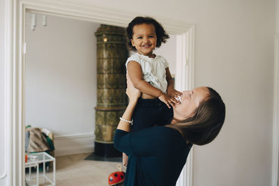 Happy mother holding daughter while standing at home