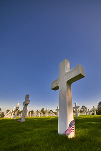 Tombstone cross on field against clear blue sky