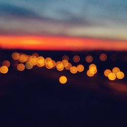 Defocused image of illuminated lights against sky at sunset