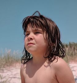 Close-up of shirtless girl looking away at beach against clear sky during sunny day