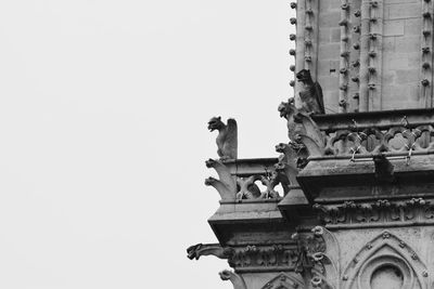 Low angle view of bird perching on statue against clear sky