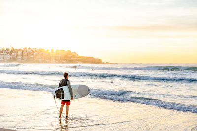 Rear view of man looking at beach during sunset