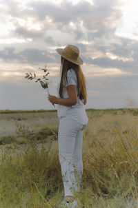 Fashion portrait of a young beautiful girl with long hair dressed in white and straw hat on field