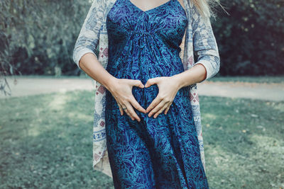 Midsection of pregnant woman making heart shape with hands