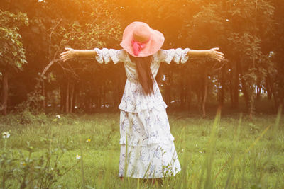 Rear view of woman with arms outstretched standing on field