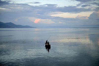 Silhouette people in boat on sea against cloudy sky during sunset