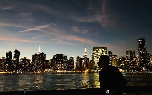 Rear view of man looking at illuminated buildings against sky