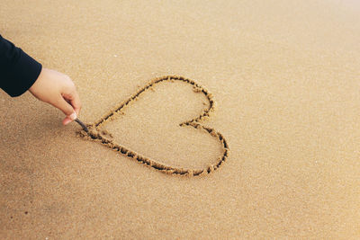 Hand holding heart shape on sand at beach