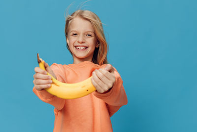 Portrait of young woman holding banana against clear blue background