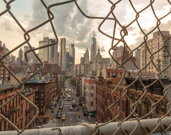 One world trade center against sky in city seen through chainlink fence