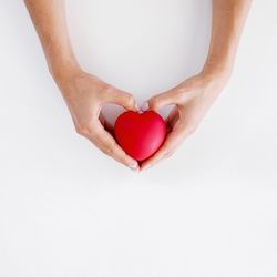 Midsection of woman holding heart shape over white background