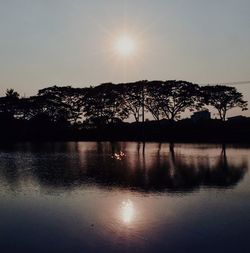 Silhouette trees by lake against sky during sunset