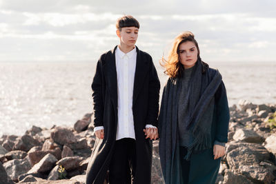 Lesbian women holding hands while standing on rock against sea and sky