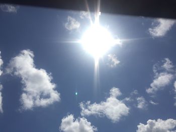 Low angle view of sun shining on cloudy sky