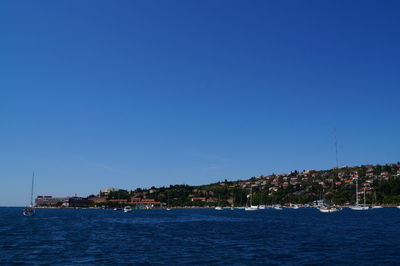 Scenic view of sea by buildings against clear blue sky