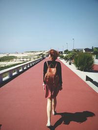 Rear view of woman walking on road against clear sky