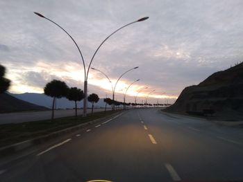 Road by trees against sky during sunset